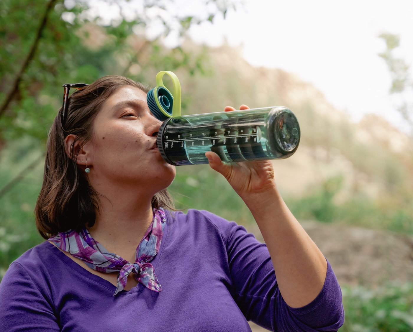 Hiker drinking from a GoBottle on a green, tree-lined trail