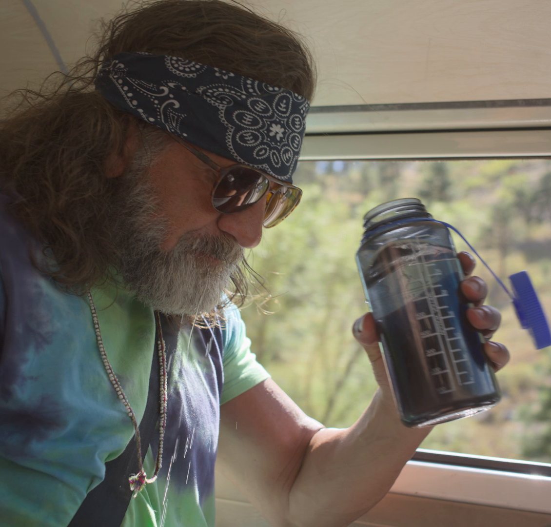 Hiker in a bandana and sunglasses holding a GoBottle beside a window